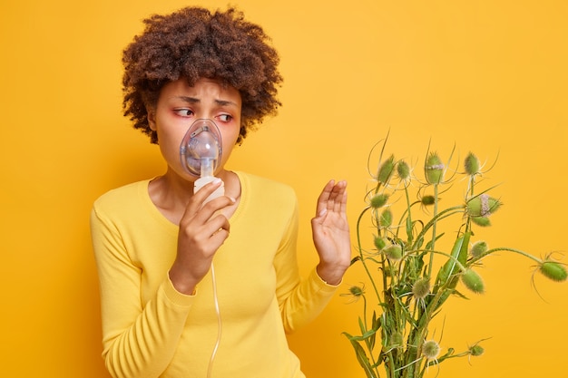 Gratis foto vrouw lijdt aan allergie voor wilde bloemen gebruikt inhalatie vernevelaar heeft rode tranende ogen reactie op stuifmeel weigert planten poseert op levendig geel