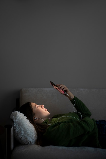 Vrouw luistert naar muziek en kijkt naar haar smartphone terwijl ze op bed ligt