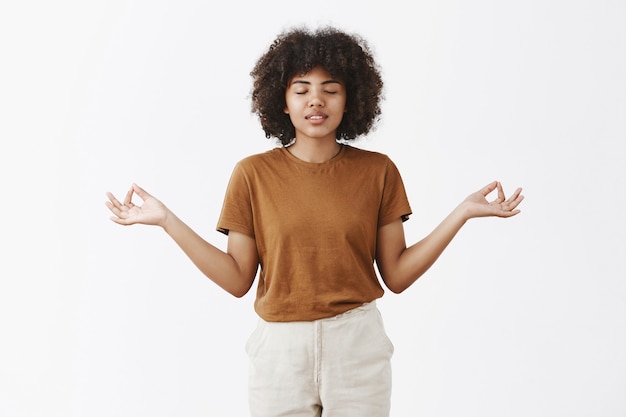 Vrouw met afro kapsel en donkere huid ogen sluiten glimlachen zorgeloos spreiden handen opzij in zen gebaar mediteren en verlichten van stress