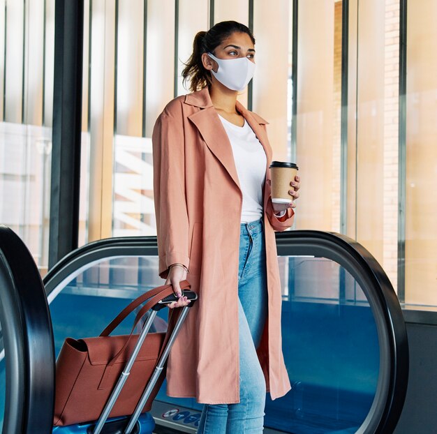 Vrouw met bagage en medisch masker op de luchthaven tijdens de pandemie