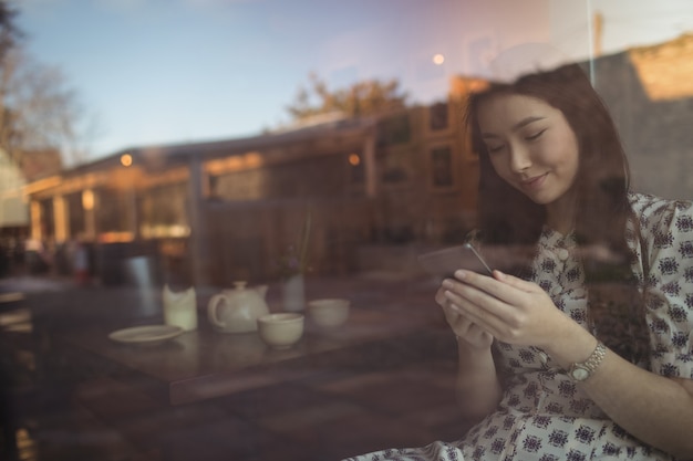 Vrouw met behulp van mobiele telefoon in de buurt van venster