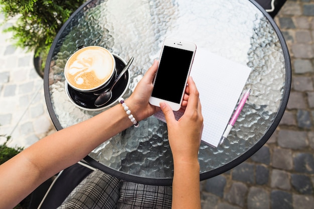 Vrouw met behulp van mobiele telefoon met een koffiekopje op de glazen tafel