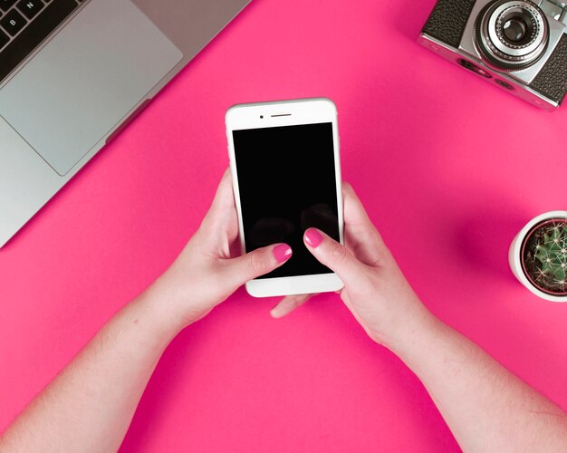 Vrouw met behulp van slimme telefoon met laptop; camera en potplant op roze achtergrond
