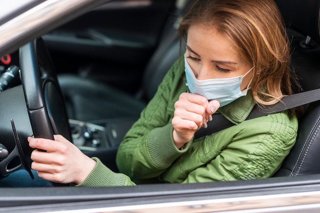 Vrouw met beschermingsmasker in haar auto het hoesten