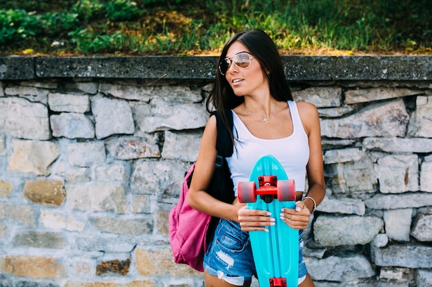 Vrouw met blauw skateboard bij de muur