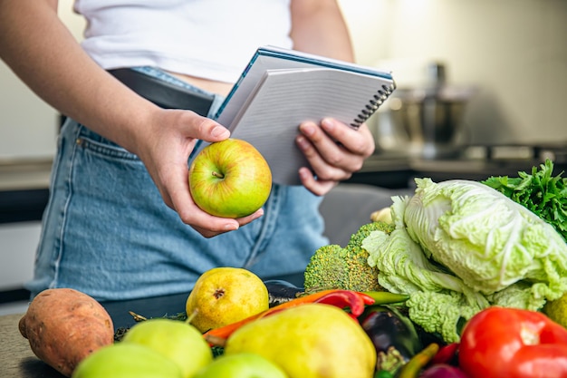 Gratis foto vrouw met blocnote en groenten op de keukentafel die een recept voorbereidt