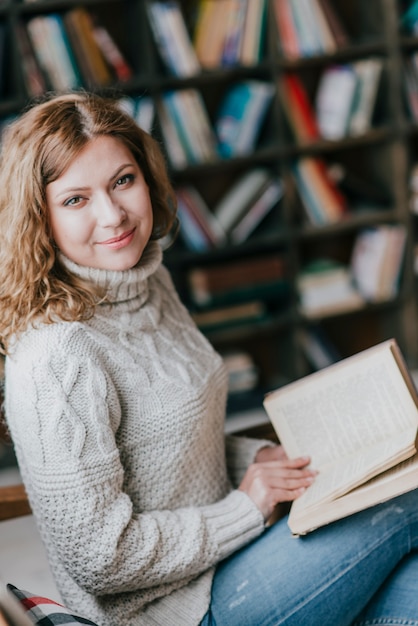 Gratis foto vrouw met boek dichtbij vage boekenkast