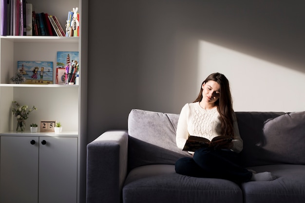 Vrouw met boek op de bank thuis