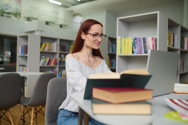 Vrouw met bril die bij laptop in bibliotheek werkt