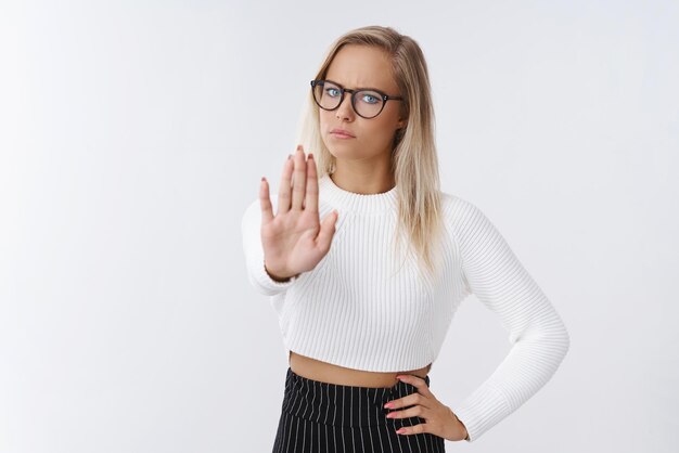 vrouw met bril en trendy outfit die handpalm naar camera trekt in verboden en geen gebaar fronsend ontevreden