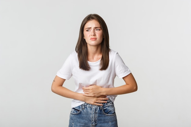 Vrouw met buikpijn, buigen en met de handen op de buik, ongemak door menstruatiekrampen.