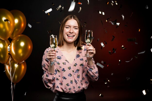 Vrouw met champagneglazen omgeven door confetti en ballonnen