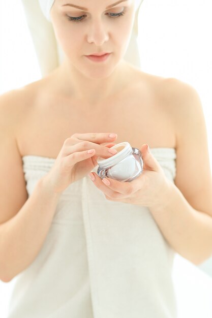 Vrouw met cosmetische producten en handdoek op haar hoofd na het douchen