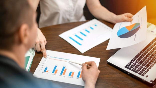 Vrouw met de diagrammen van een man-financiën op de tafel. Laptop, papieren