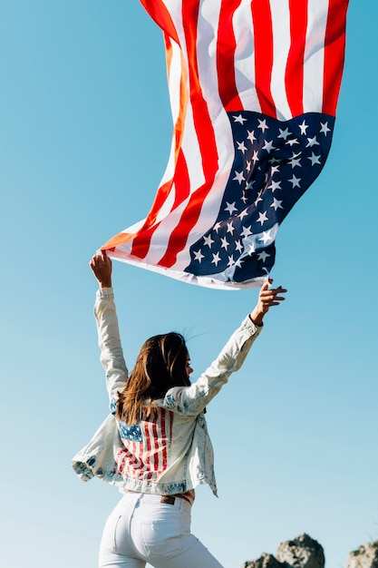 Vrouw met de golvende vlag van de VS op blauwe hemel