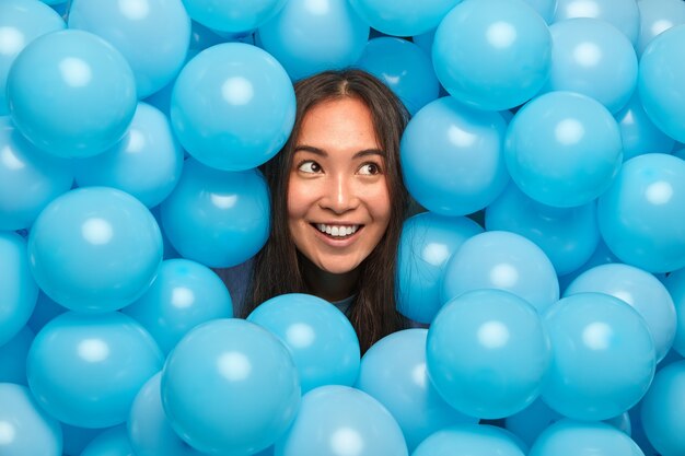 vrouw met donker haar geniet van vakantieviering kijkt opzij bedachtzaam omringd door vele opgeblazen blauwe ballonnen