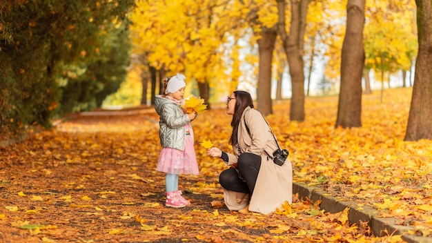 Vrouw met een babymeisje loopt in het herfstpark en maakt foto's tegen de achtergrond van felgeel herfstgebladerte