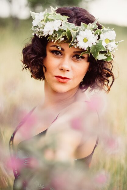 Vrouw met een bloemenkrans op haar hoofd poserend in een veld