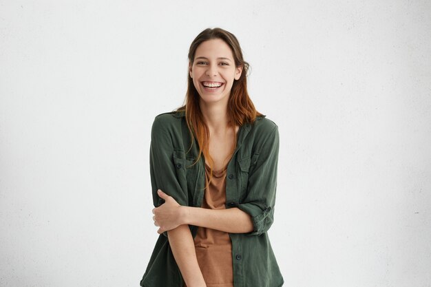 vrouw met een brede glimlach gekleed in een groene jas en een bruin T-shirt glimlachend in het algemeen blij je te ontmoeten