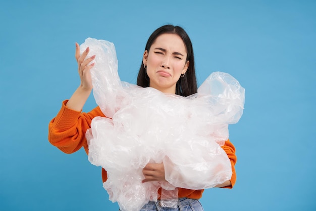 Vrouw met een geërgerd onwillig gezicht dat veel plastic afval laat zien, heeft een hekel aan recycling als ze over blauwe b