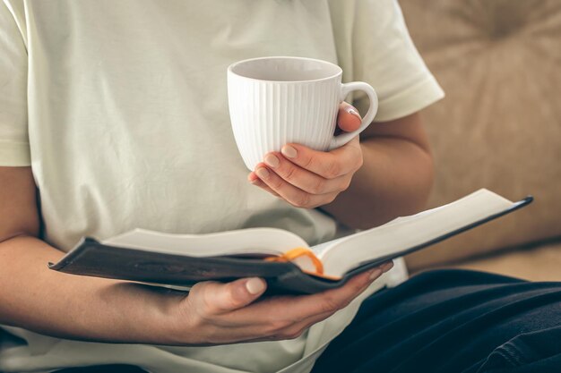 Gratis foto vrouw met een kop thee en een boek aan het lezen op de bank thuis dichtbij