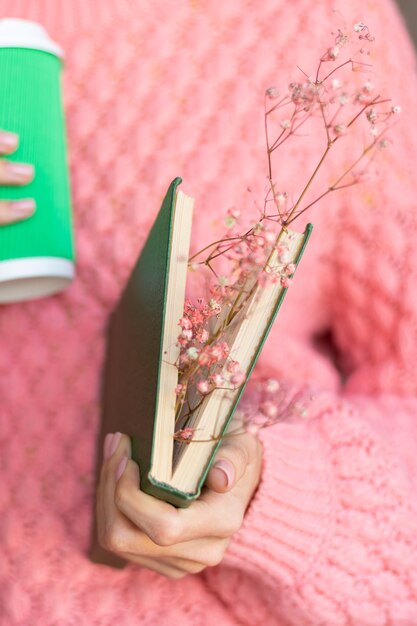 Vrouw met een opengeslagen boek met een boeket gedroogde bloemen erin en een papieren kopje koffie