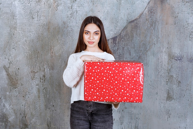 vrouw met een rode geschenkdoos met witte stippen erop.