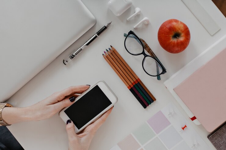 Gratis Foto vrouw met een smartphone aan het bureau met potloden, een bril en een laptop
