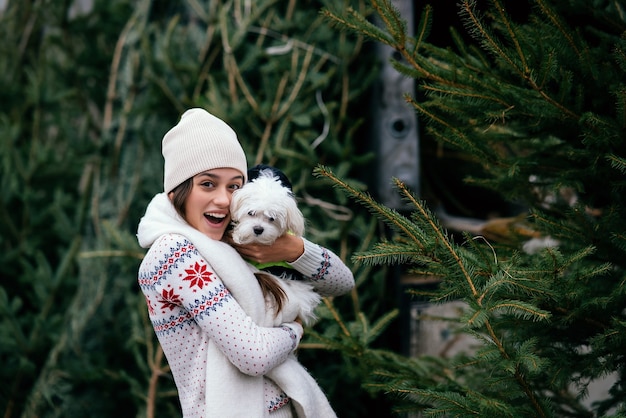 Vrouw met een witte hond in haar armen bij groene kerstbomen op de markt