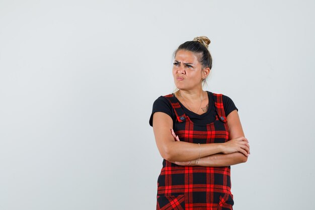 Vrouw met gekruiste armen in schort jurk en aarzelend op zoek. vooraanzicht.