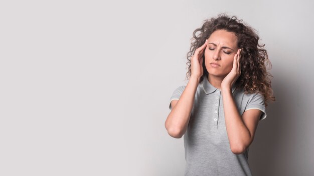 Vrouw met gesloten ogen die aan hoofdpijn tegen grijze achtergrond lijden