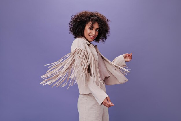 Vrouw met golvend haar danst op paarse achtergrond Brunette krullende vrouw in beige outfit poseren en bewegen op geïsoleerde backdrop