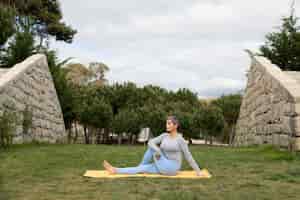 Gratis foto vrouw met grijs haar die yoga in park doet. vrouwelijk model in sportieve kleding oefenen op mat op bewolkte dag. sport, hobby, gezondheidsconcept