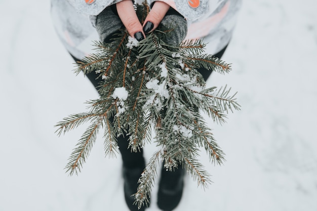 Vrouw met groene pijnboomtakken met sneeuw op onscherpe achtergrond