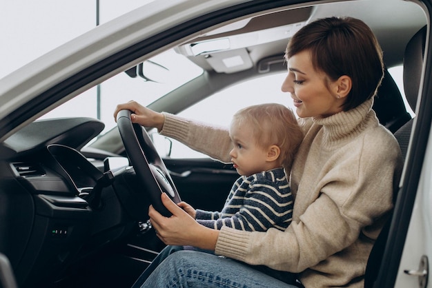 Vrouw met haar zoontje met stuurwiel in een auto in een autoshowroom