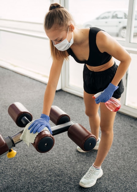 Gratis foto vrouw met handschoenen en medisch masker op de desinfecterende uitrusting van de sportschool