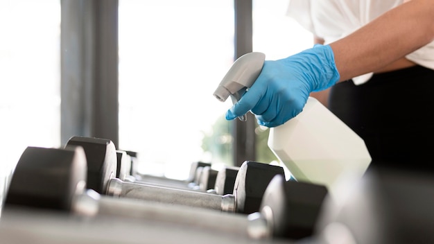 Vrouw met handschoenen en reinigingsoplossing gym gewichten desinfecteren