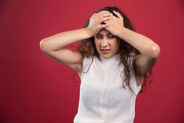 Vrouw met hoofdpijn die haar hand op het hoofd op rood houdt.