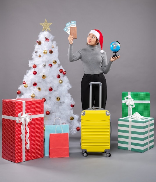 Gratis foto vrouw met kerstmuts met bagage naast de kerstboom
