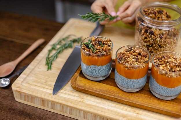 Vrouw met kleurrijke gezonde zoete woestijnen chia puddingen gemaakt van amandelmelk, blauwe spirulina-extract, chiazaad, pappaya-mangocam en zelfgemaakte granola. Op houten tafel in de keuken thuis.