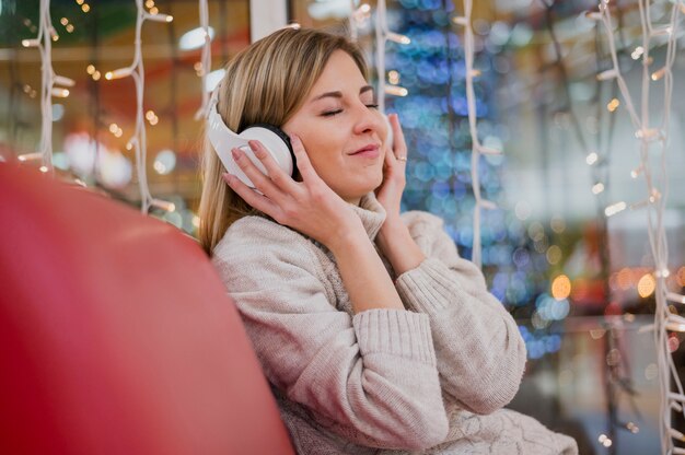 Vrouw met koptelefoon op hoofd en zittend op de bank in de buurt van kerstverlichting