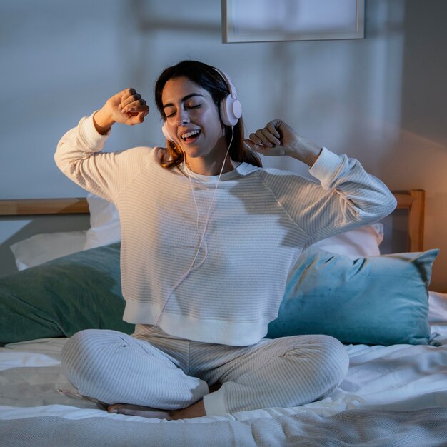 Vrouw met koptelefoon voor muziek thuis in bed