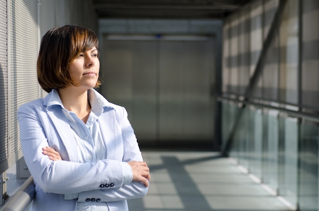 Vrouw met kort haar, gekleed in een wit overhemd dat zich dichtbij de glazen van een viaduct bevindt