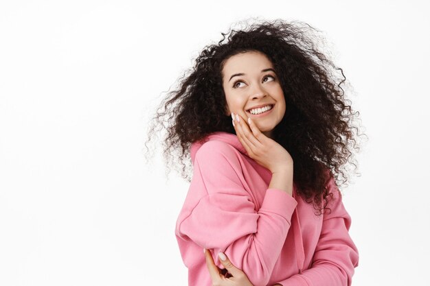 vrouw met krullend donker haar, haar gezicht aanrakend, glimlachend en opzij starend naar wit