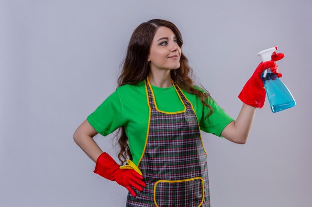 vrouw met lang golvend haar die een schort en rubberen handschoenen draagt die schoonmaakspray houdt die er zelfverzekerd uitziet klaar om schoon te staan