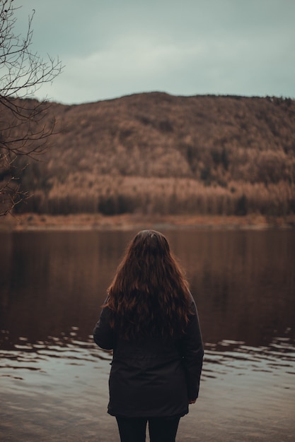 Gratis foto vrouw met lang rood haar dat zich dichtbij een meer in een bos bevindt