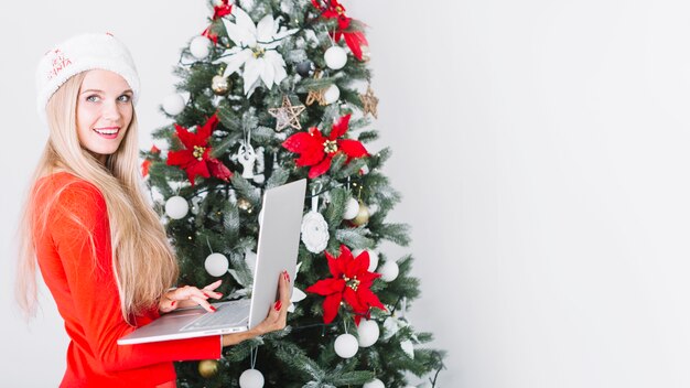 Vrouw met laptop dichtbij Kerstboom