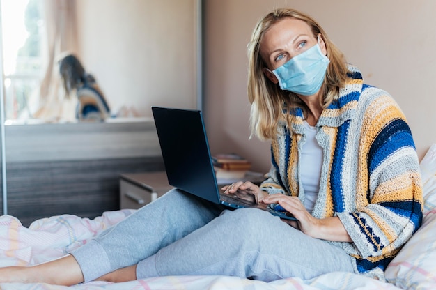 Vrouw met laptop en medisch masker in quarantaine thuis