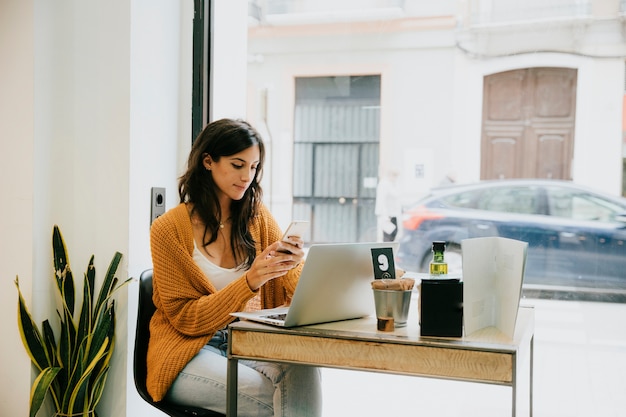 Gratis foto vrouw met laptop en smartphone in café