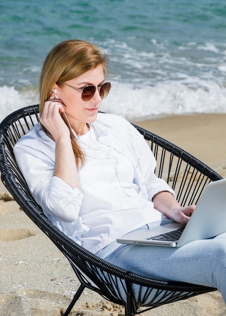 Gratis foto vrouw met laptop en zonnebril die bij het strand werken